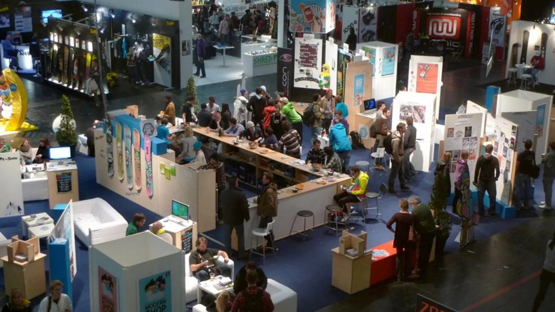 Messestand mit Besuchern, Tischen und Ständen im Hintergrund