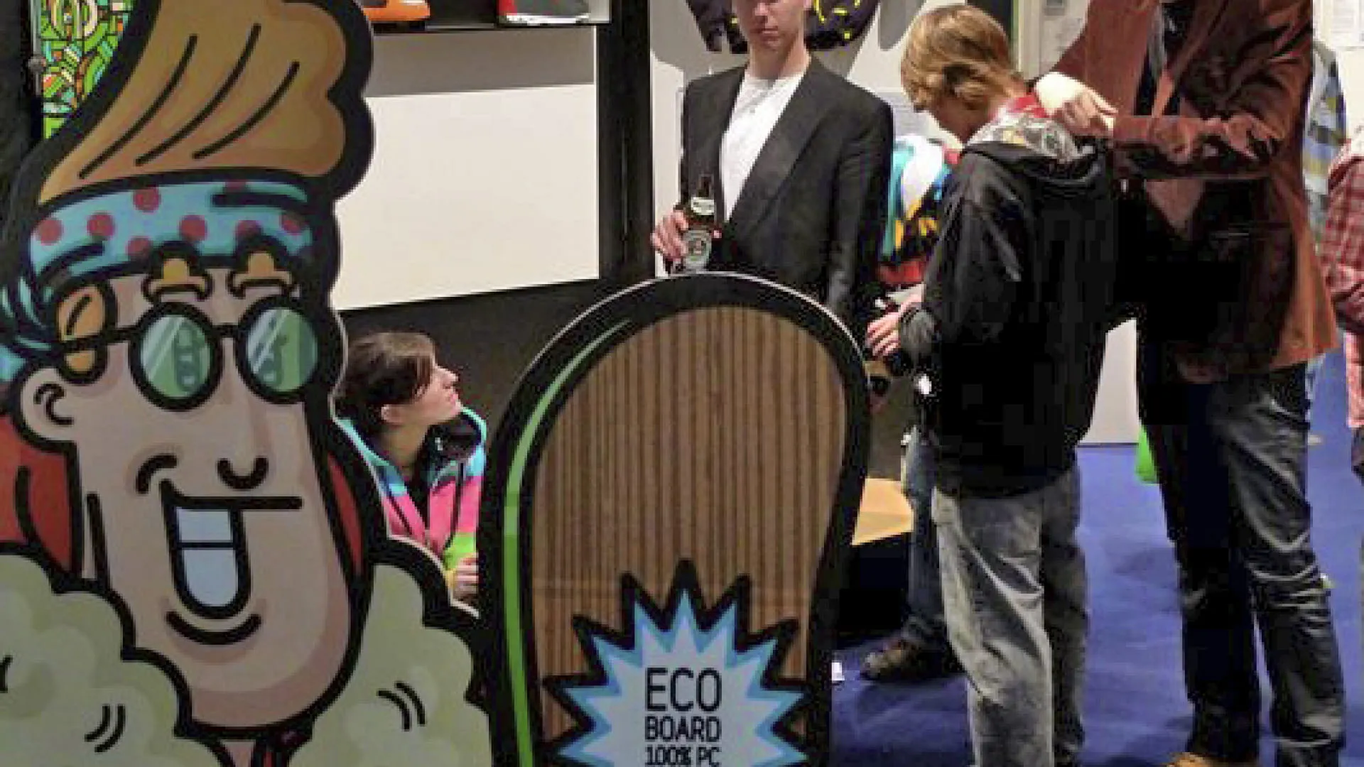 Messestand mit Skaterfiguren und Menschen, Skateboards im Vordergrund