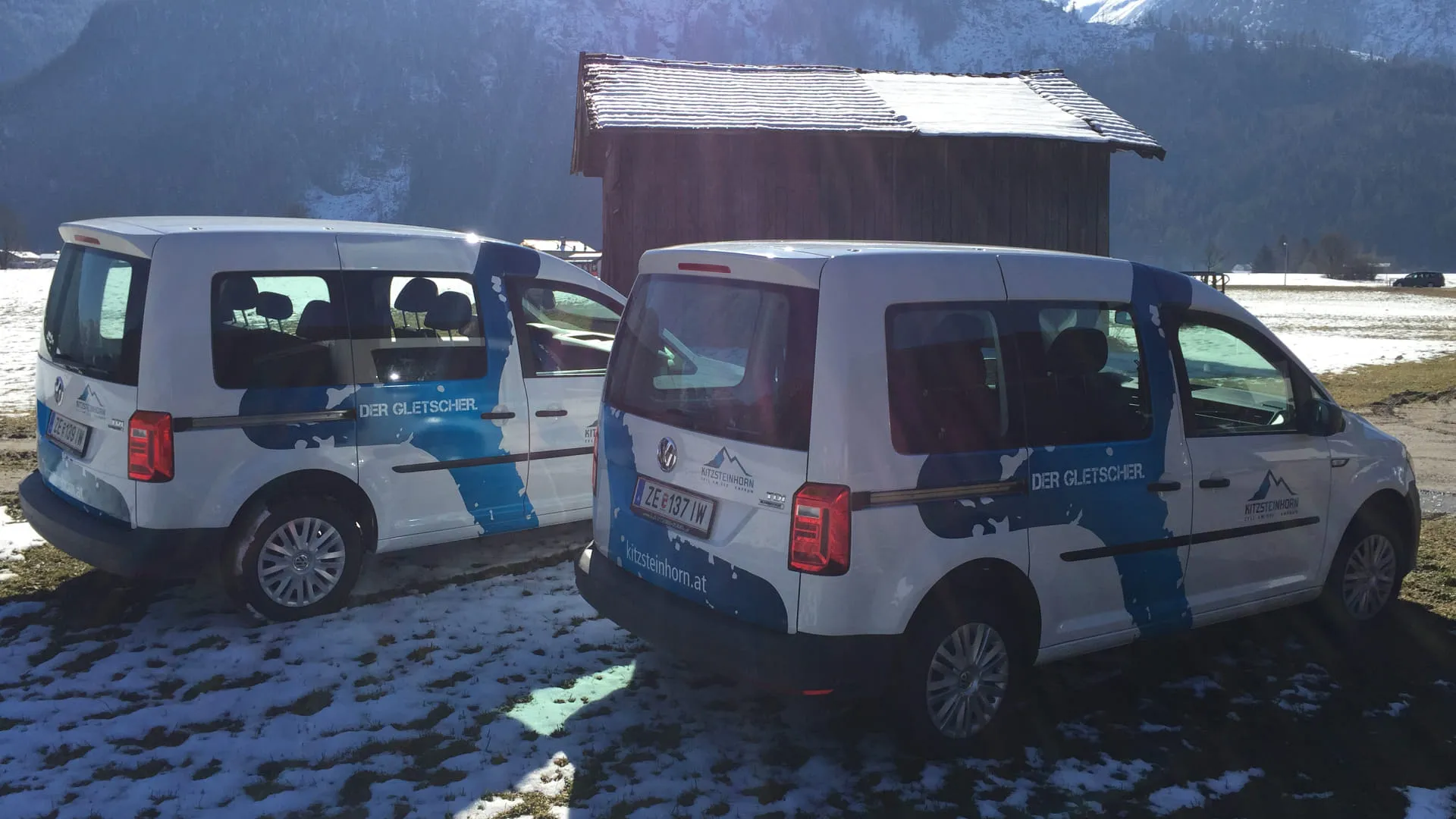 Zwei Autos auf Schnee vor einer Hütte in den Bergen.